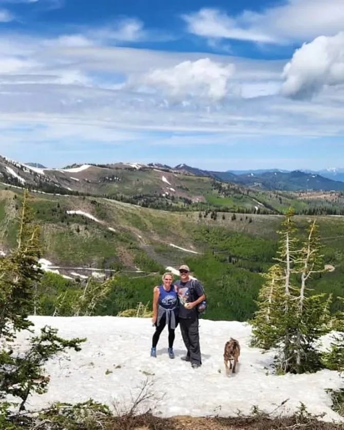 Travel advisor Shannon standing on snowy ground with male companion and dog with green mountains in view