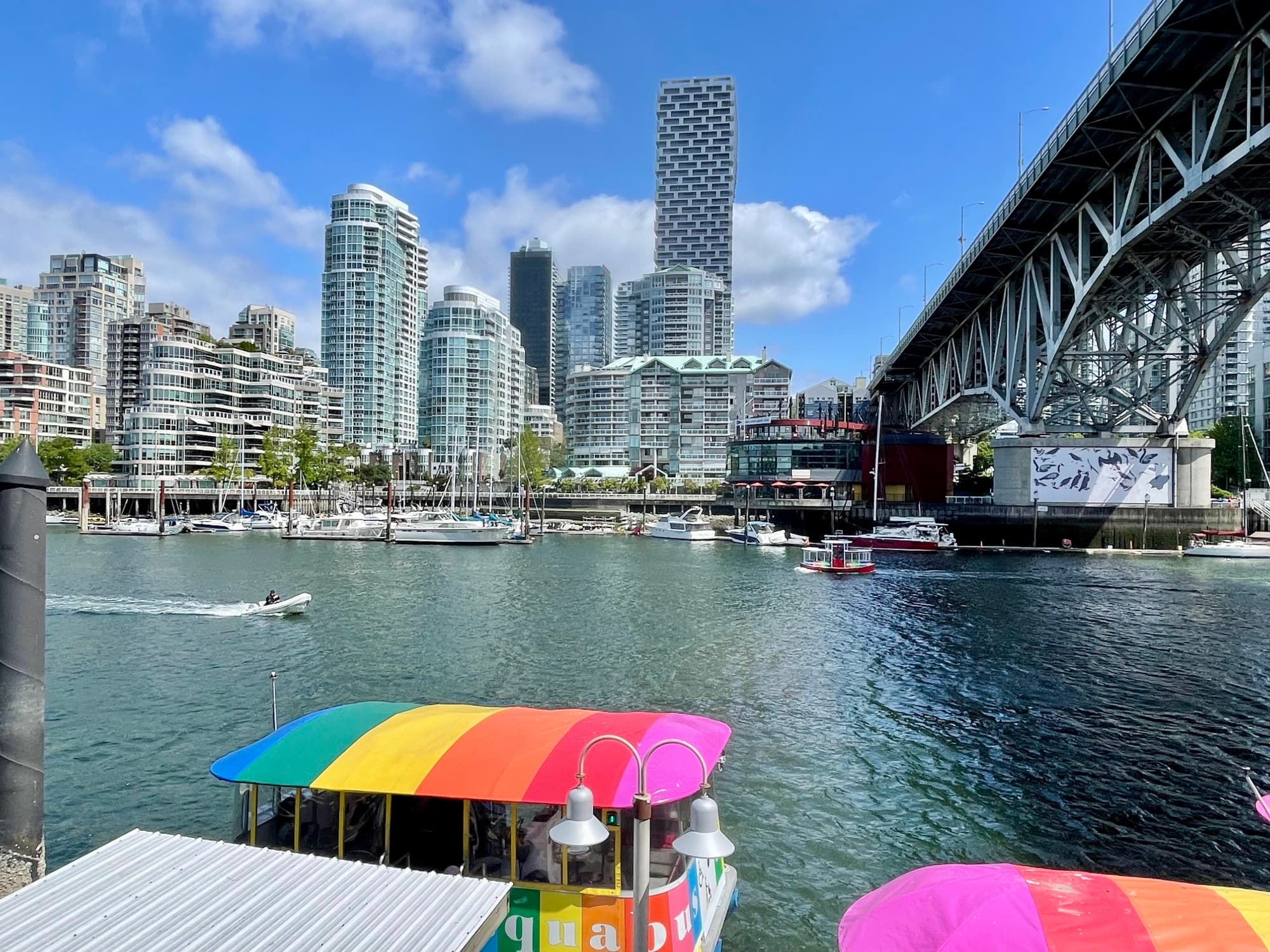 Skyrocketed buildings beside the river and boats floating with rainbow rooftops.