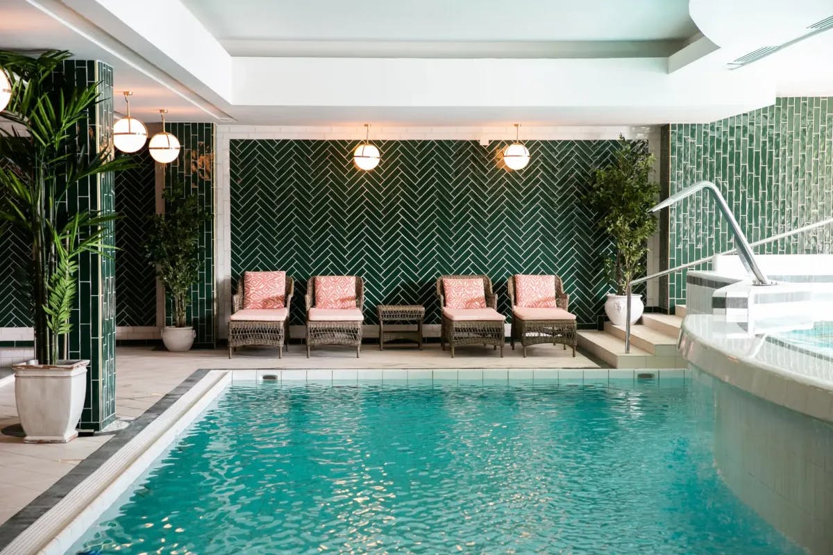 pink loungers in front of green tiled walls in a room with an indoor pool 