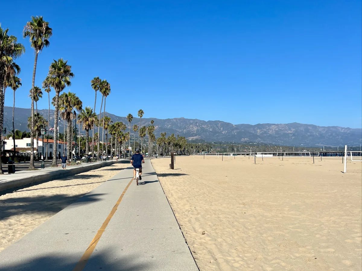 Santa Barbara beach trail with joggers, bikers and volleyball nets on the beach in the distance. 