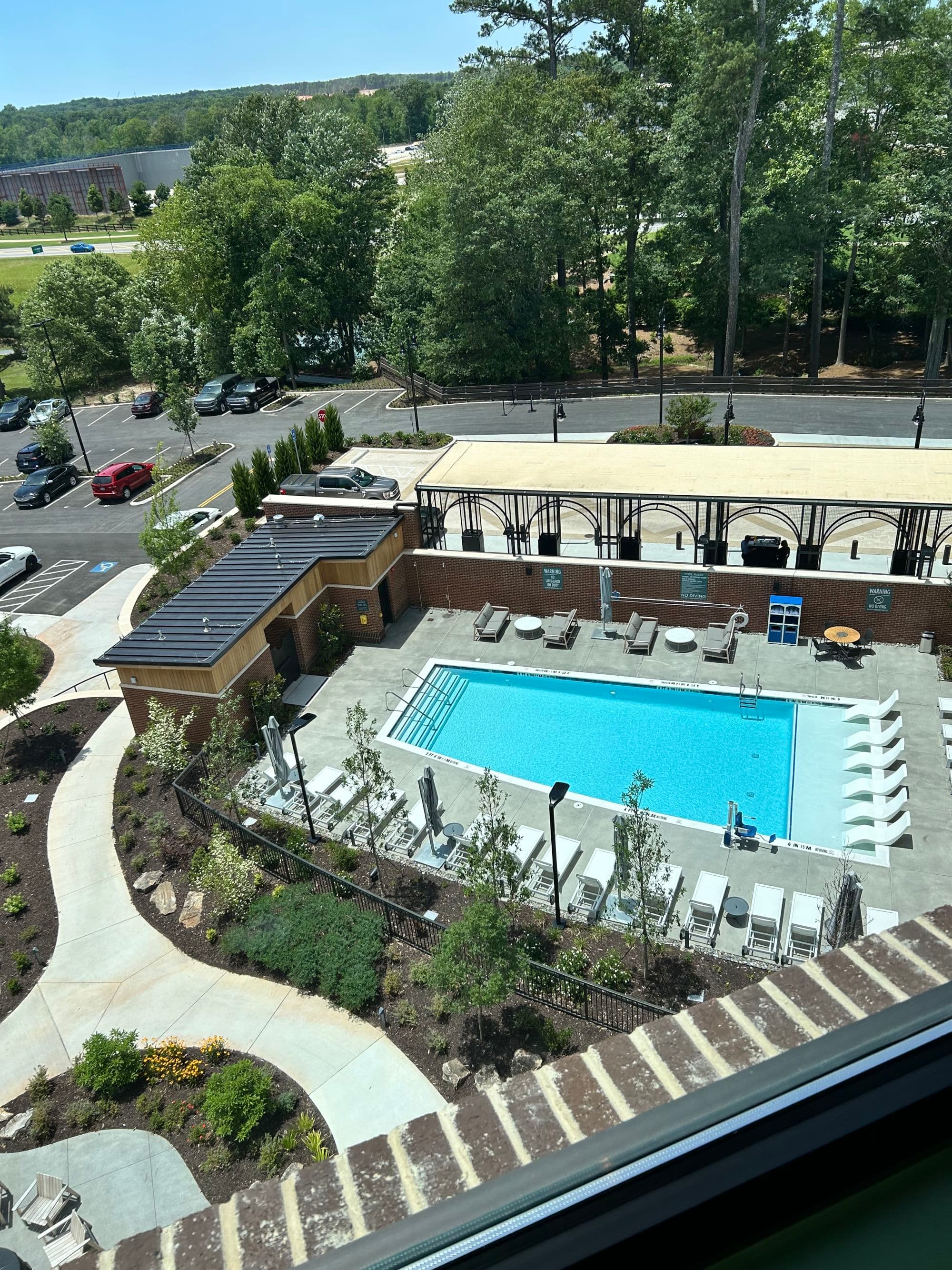 Pool view on a sunny day with foliage and seating.