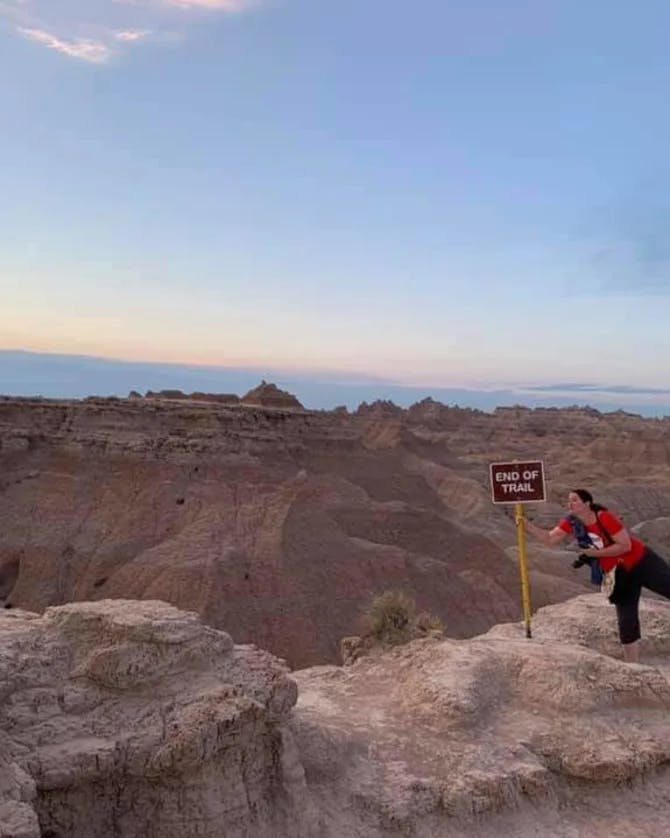 Travel advisor holding a board saying End of Trail on hills. 