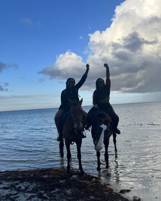 Two people riding horses on the ocean shore. 