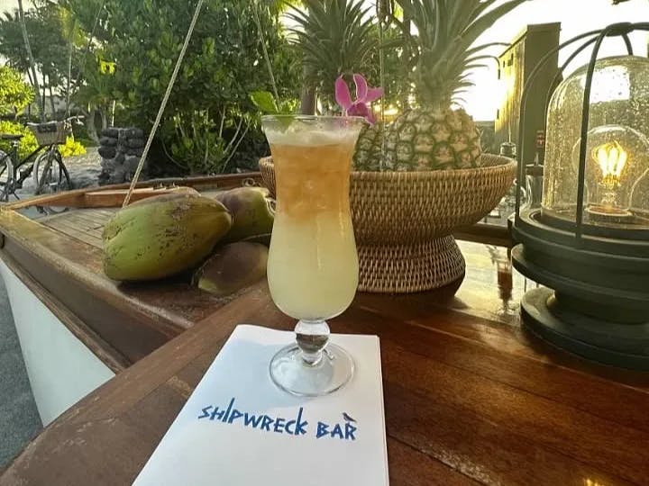 A yellow cocktail on a brown table outdoors.