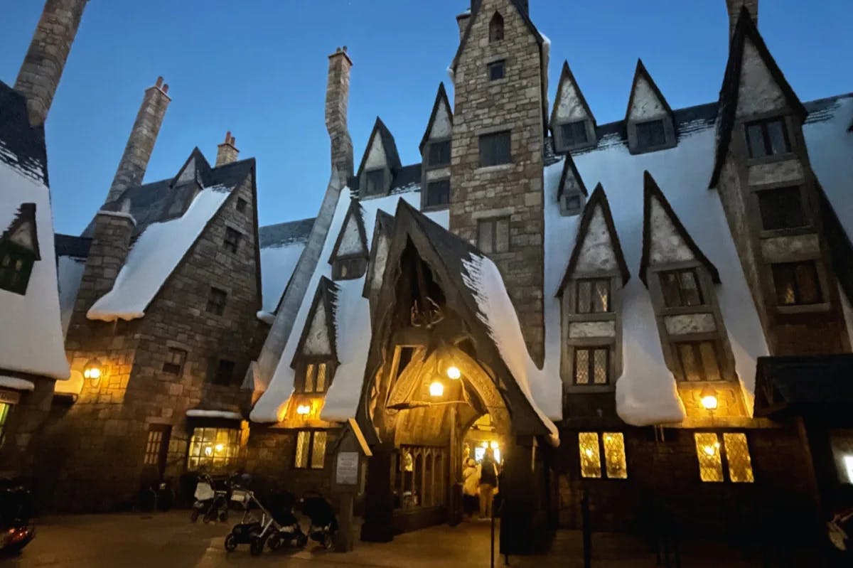 A picture of the Three Broomsticks building complete with an A-framed house and snow covered roofing. There are lit lanterns on the outside. 