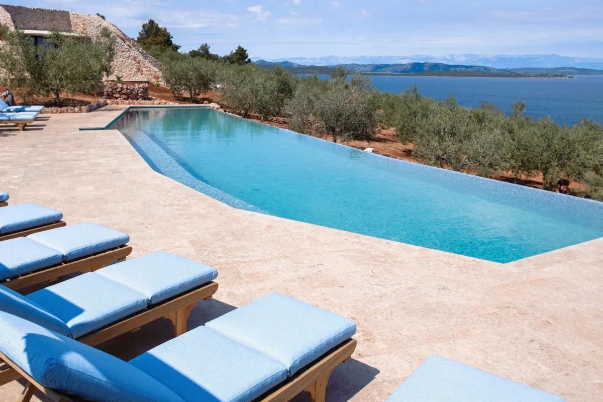 blue infinity pool with stone terrace and loungers overlooking the sea