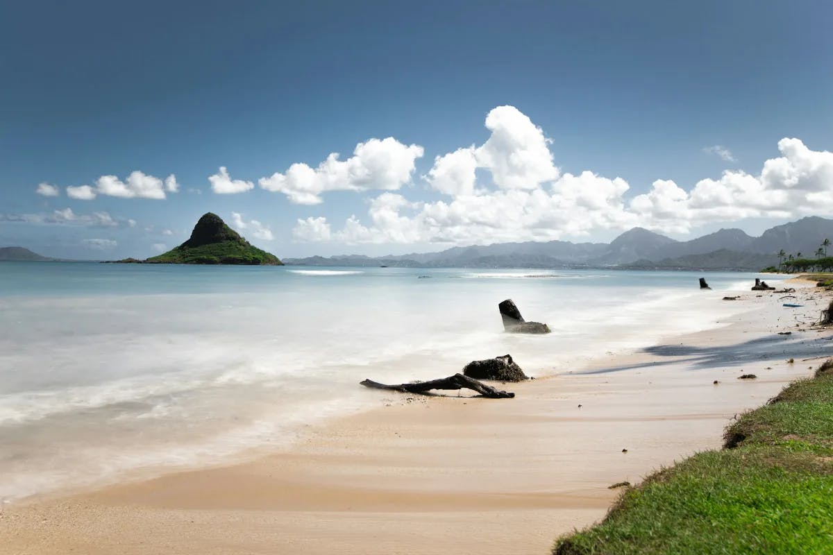 A golden beach with blue waves and a mountain in the distance.