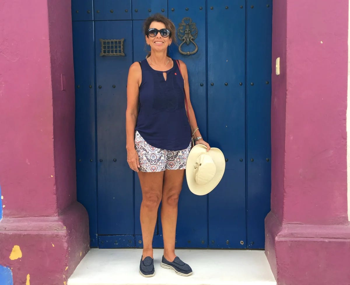 A casual summer vibe: an individual stands before a striking blue door set in a pink wall, exuding relaxed charm.