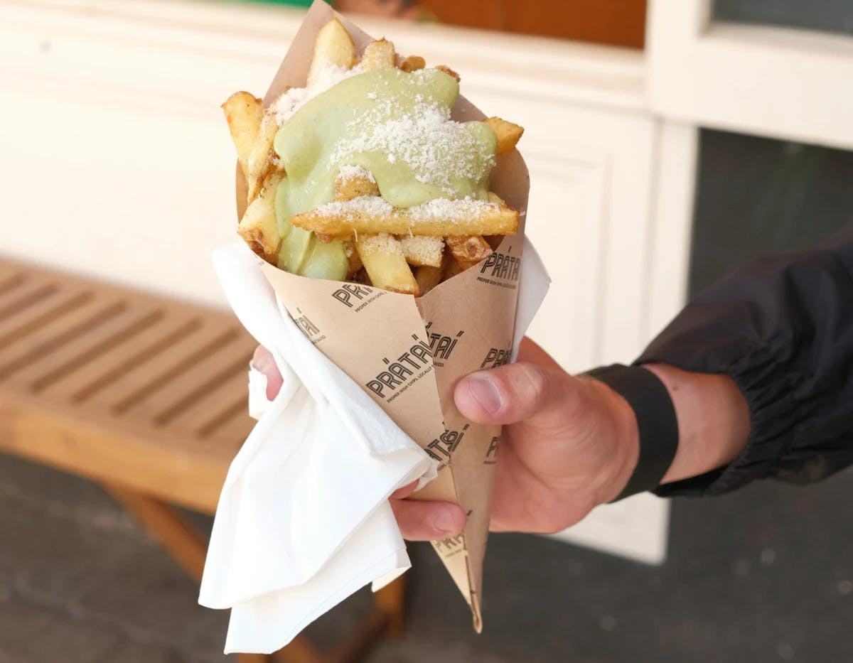 A person's hand holding fries in a paper cone smothered in sauce