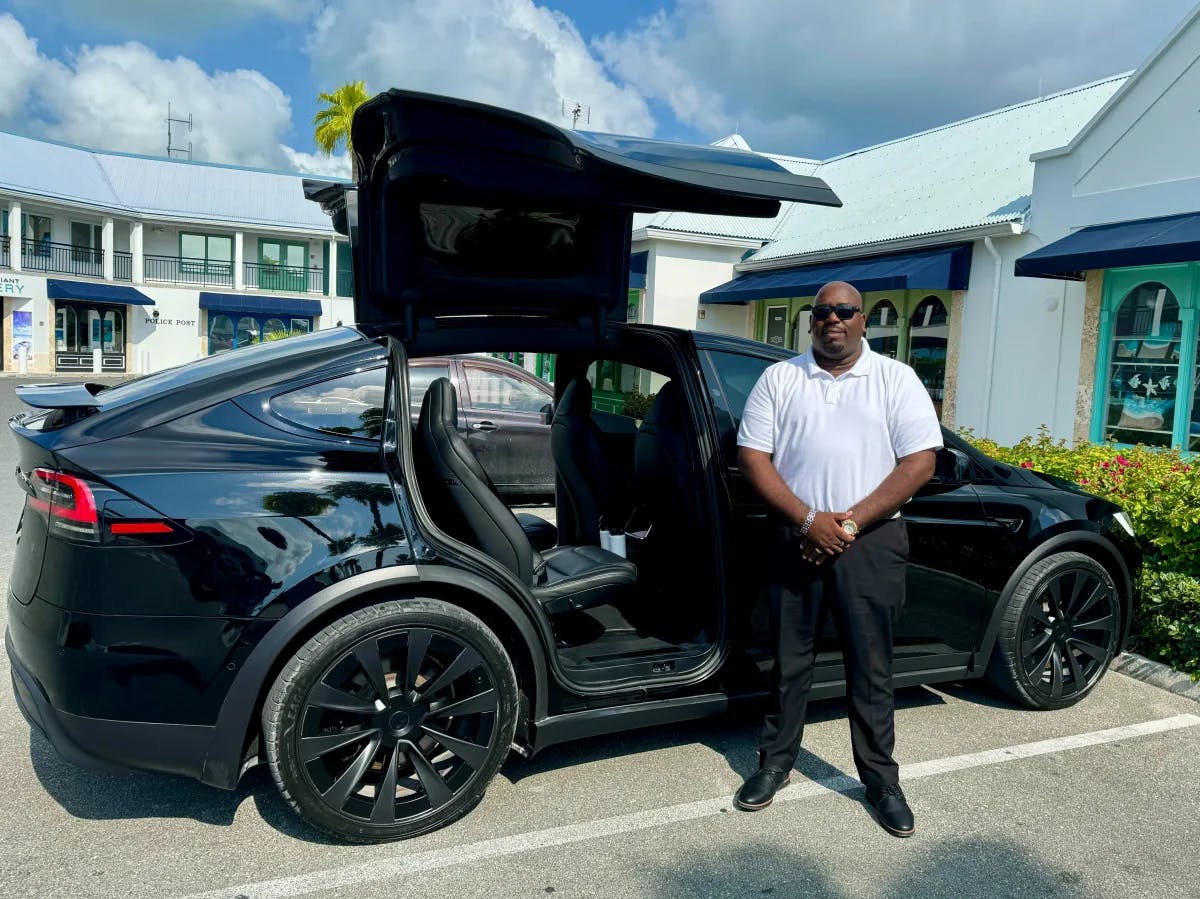 The image portrays a person standing proudly next to a sleek black Tesla with its distinctive falcon wing door open.