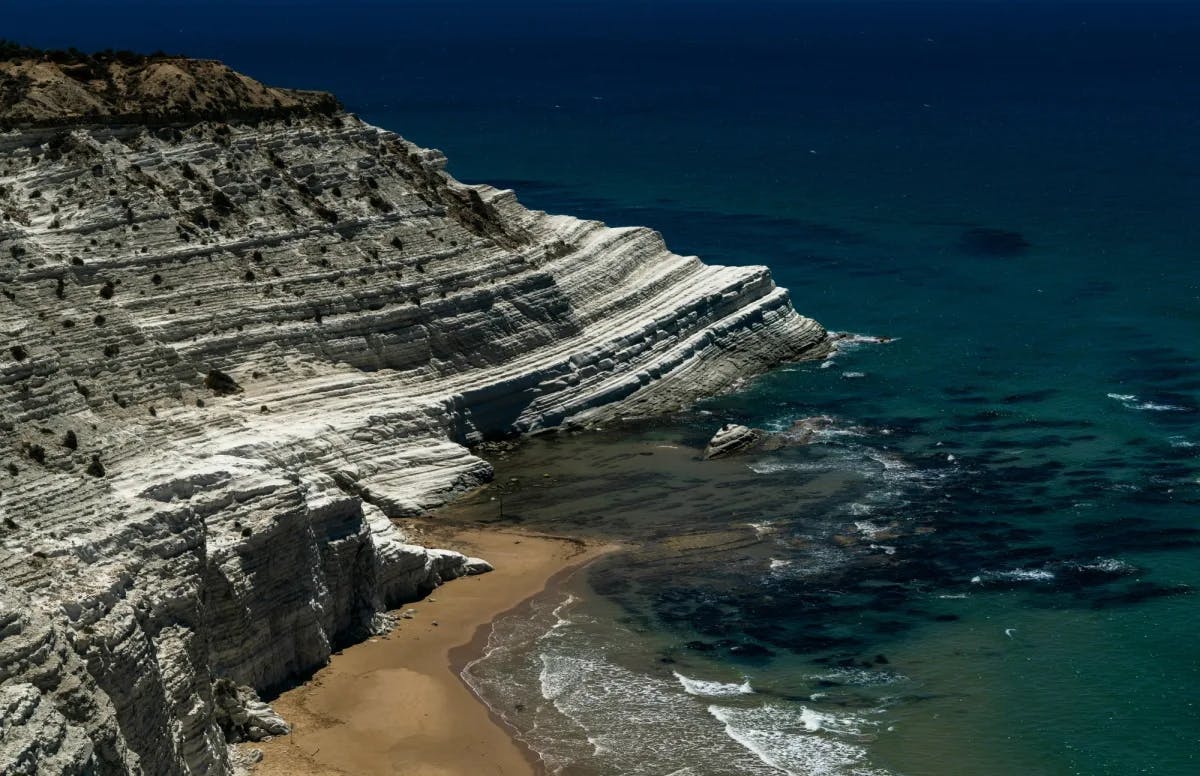 White rocky mountain and sandy beach beside a dark blue sea. 