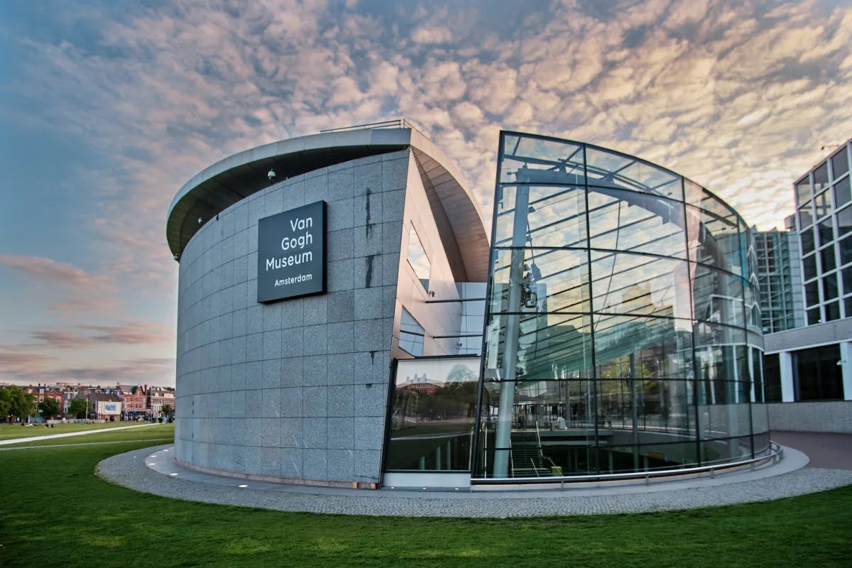 A look at the exterior of the round, half stone, half glass Van Gogh Museum underneath a pinkish sunset. 