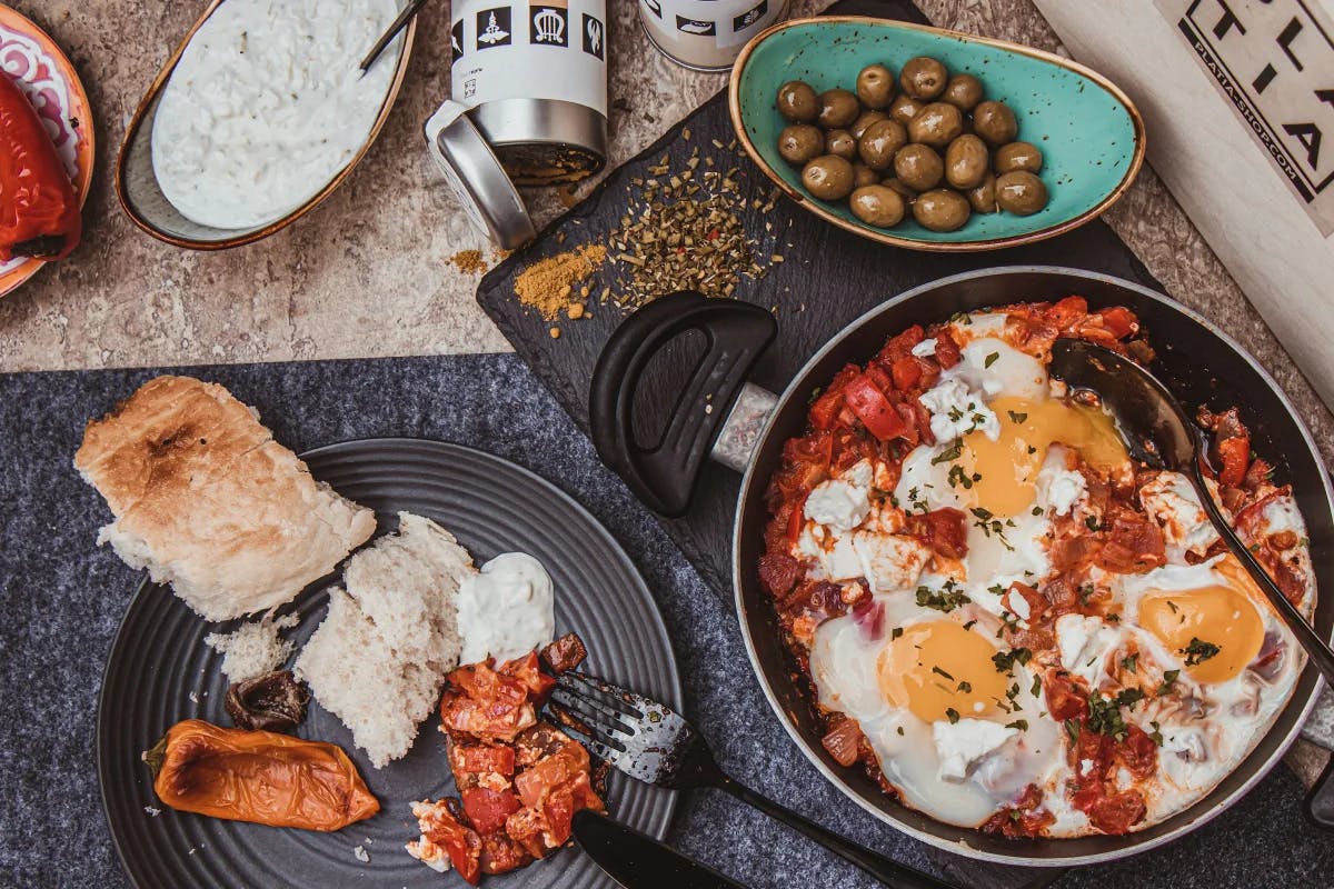 A flat-lay selection of Mediterranean food, including olives and baked eggs.