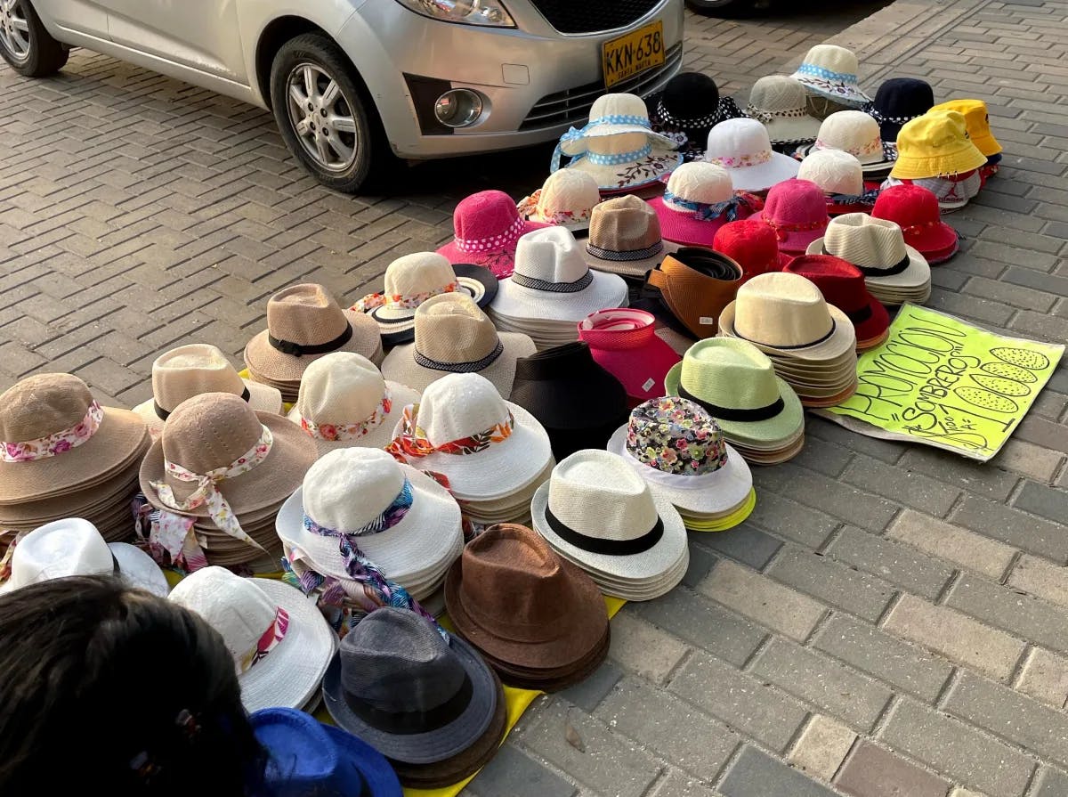 A colorful display of hats for sale, laid out on the ground in a parking lot with cars in the background.