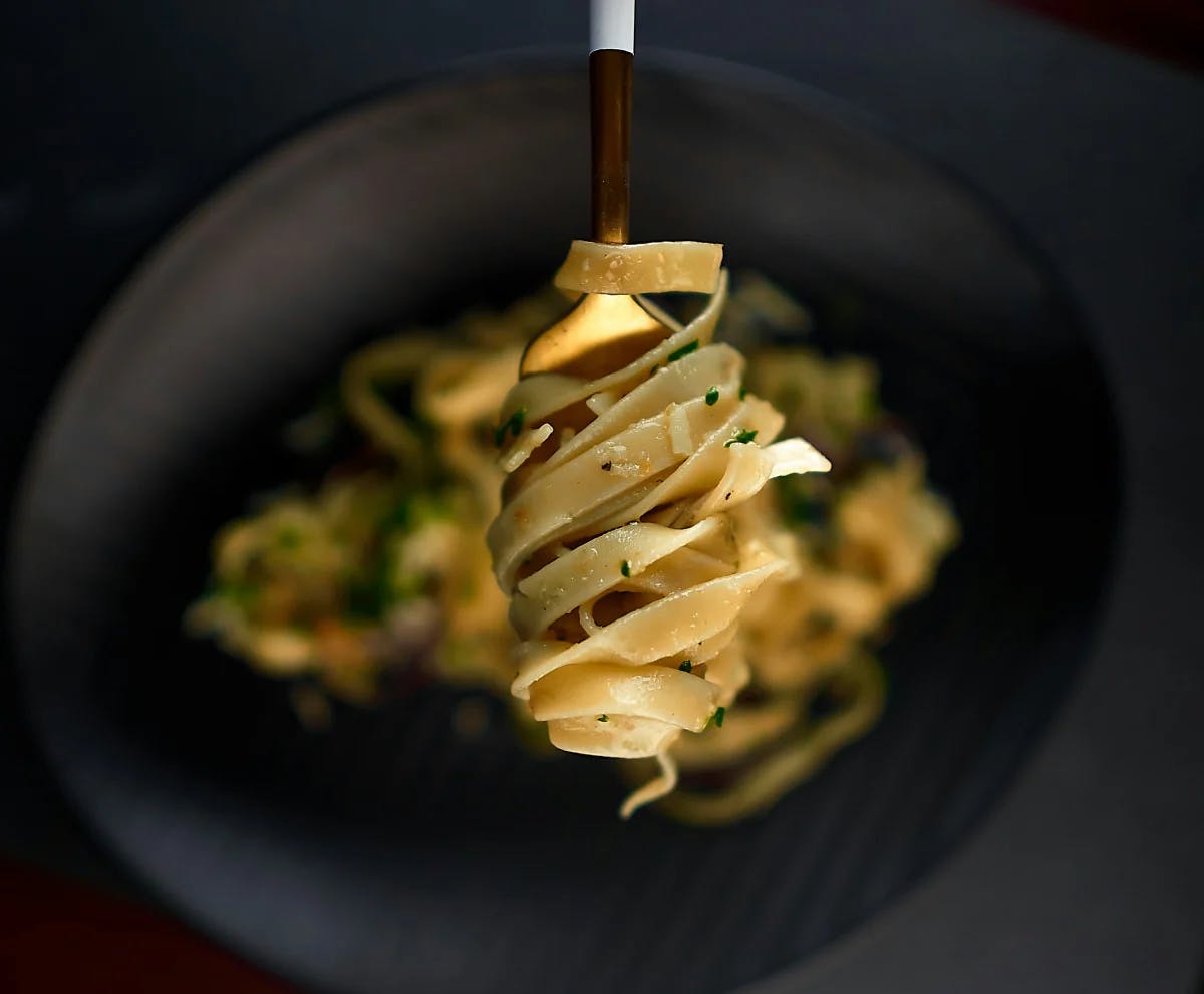 Pasta on a fork over a black plate on a black table.