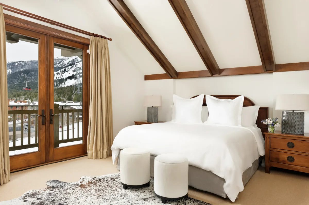 a plush white bed atop a cowhide rug in a hotel room overlooking a ski mountain