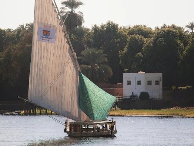 A sailboat on the Nile with grass and trees on the banks