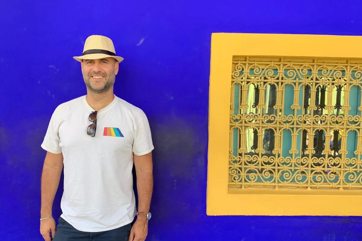 a man in a hat stands next to a yellow frame on a blue wall