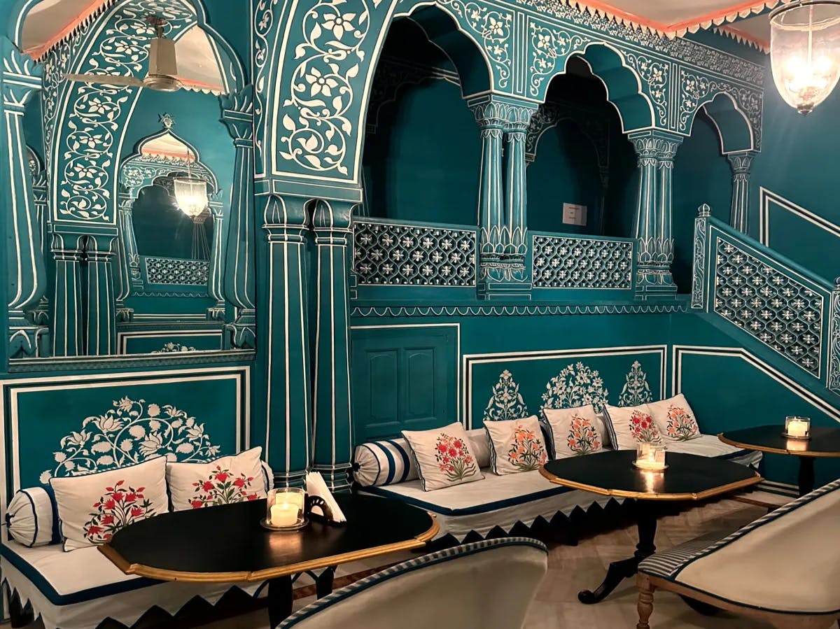 A beautiful interior showcasing intricately detailed turquoise walls, pendants and seating with beautiful and decorative pillows, tables and tiled flooring. 