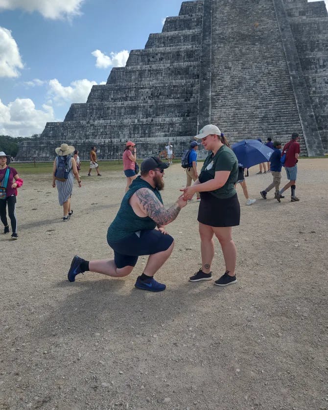 Two people standing outside of ancient ruins and the man is proposing to a woman.