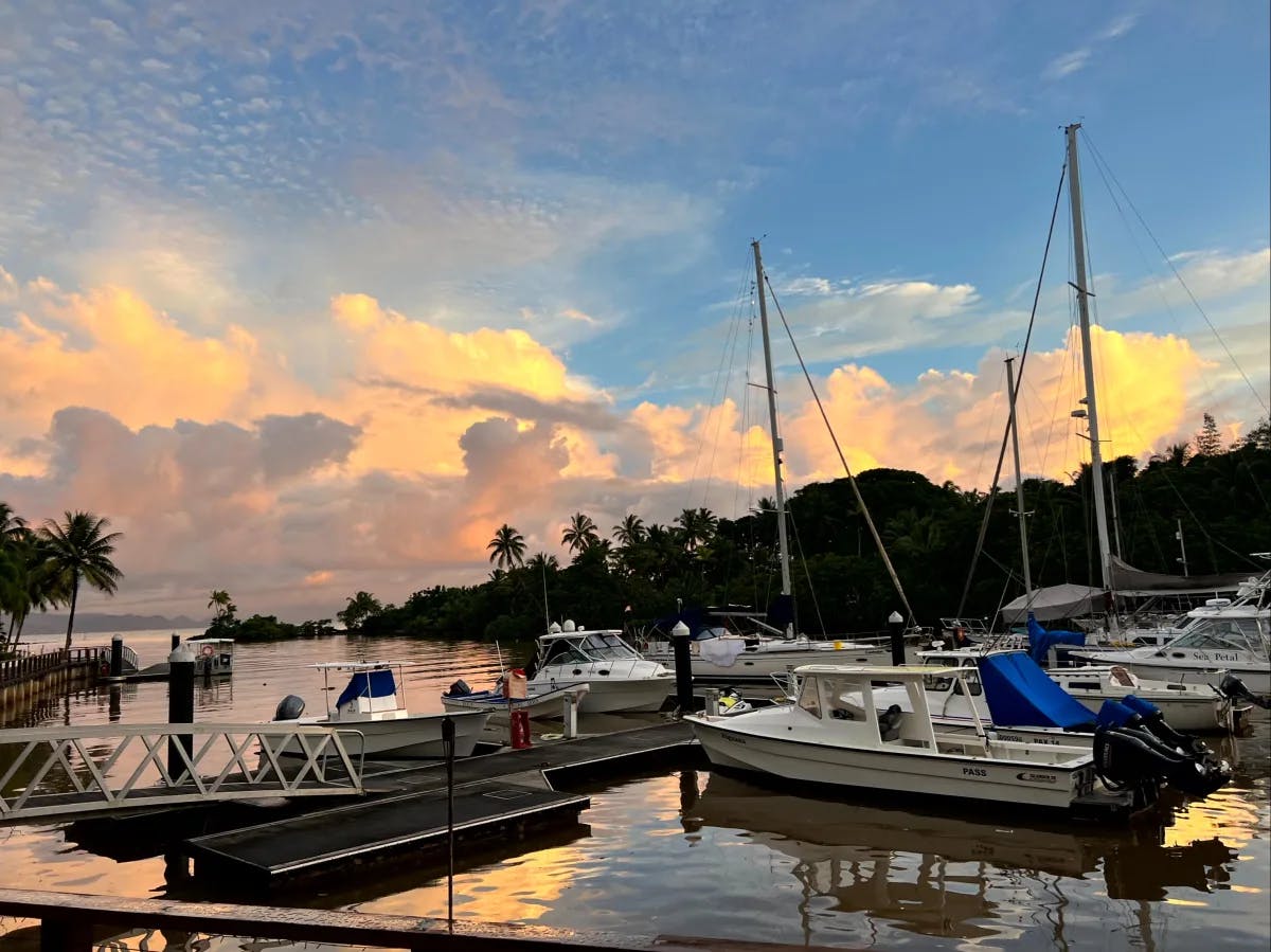 A serene marina with boats docked at sunset, highlighted by vibrant sky colors and water reflections.