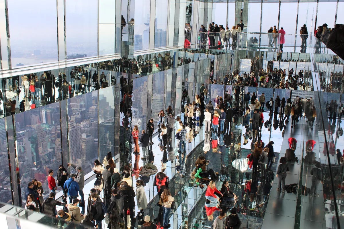 A view of people walking around a reflective building with large glass windows and mirrored walls. 