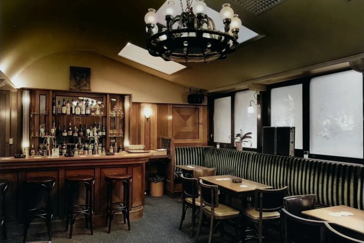 The interior of Cafe Schiller, with a wooden bar, black-and-white booths and a large chandelier.