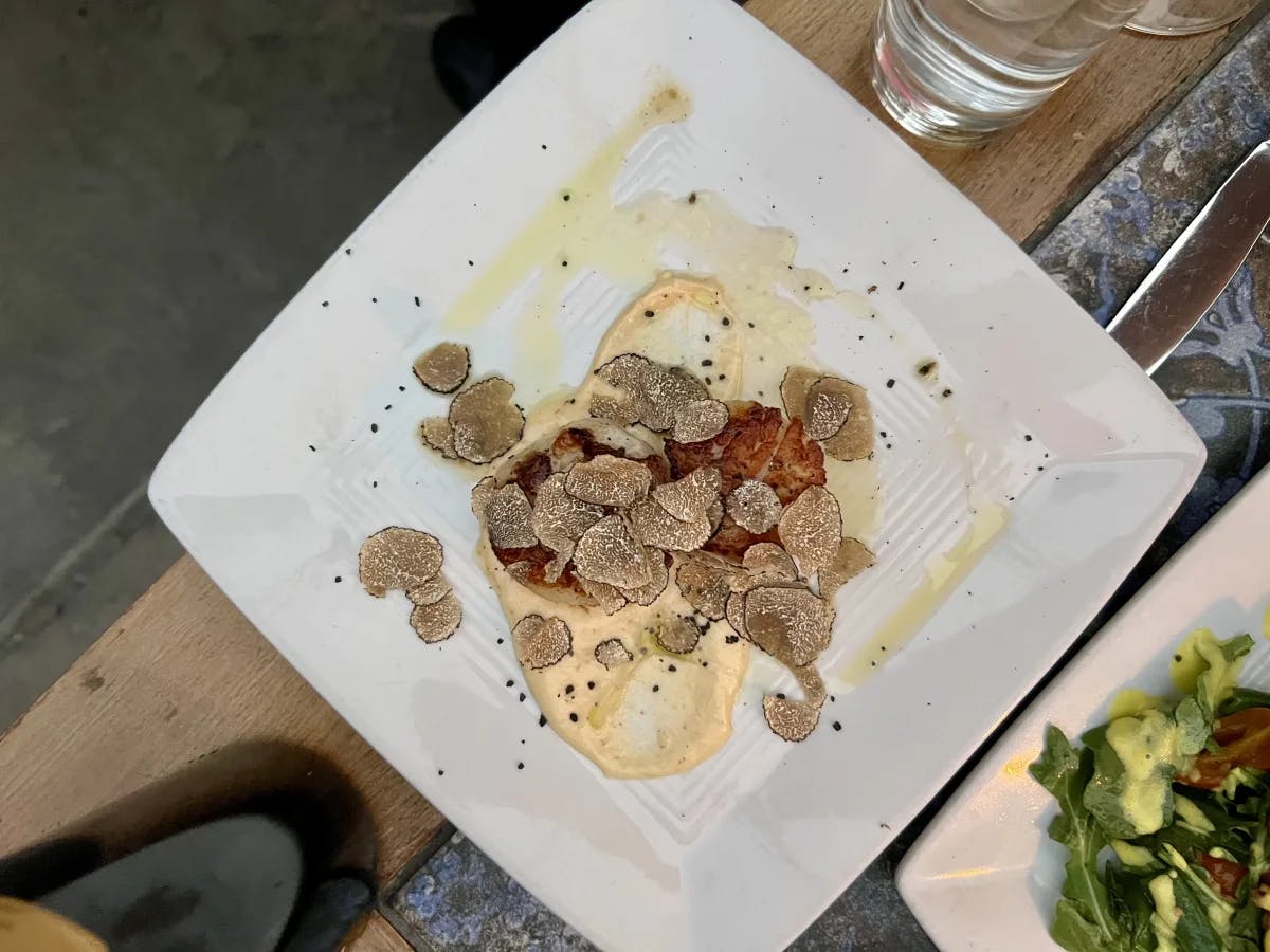 Scallops and Freshly Shaved Truffle from Barrique Venice on a white plate with water glasses in the surrounding area.