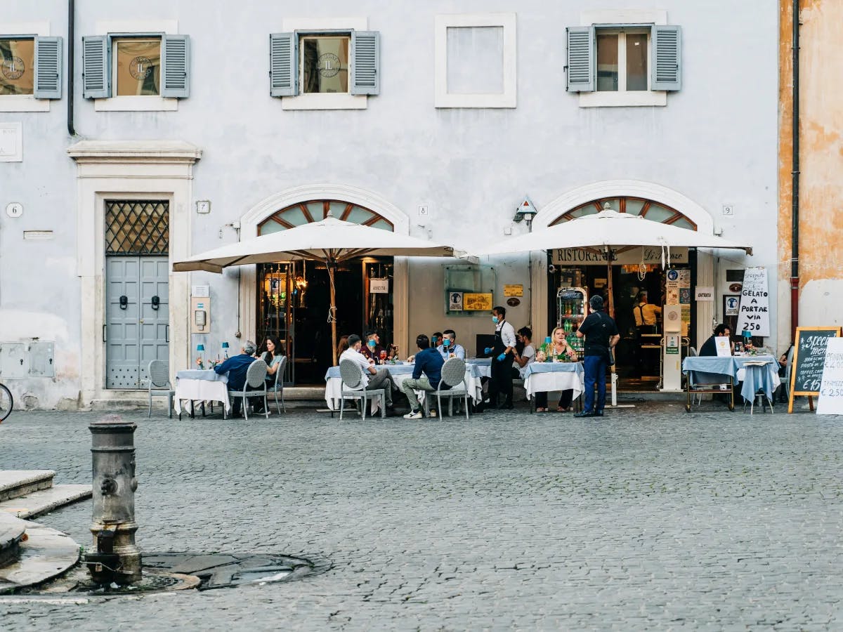 The image portrays a lively outdoor dining scene in a European setting, complete with restaurant patrons enjoying their meals.