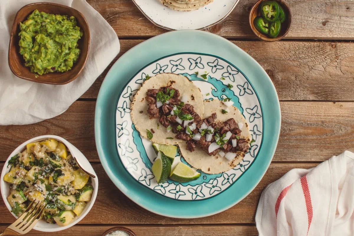 A tantalizing display of tacos and guacamole on a rustic table, accompanied by a cheesy side dish and fresh chilies.