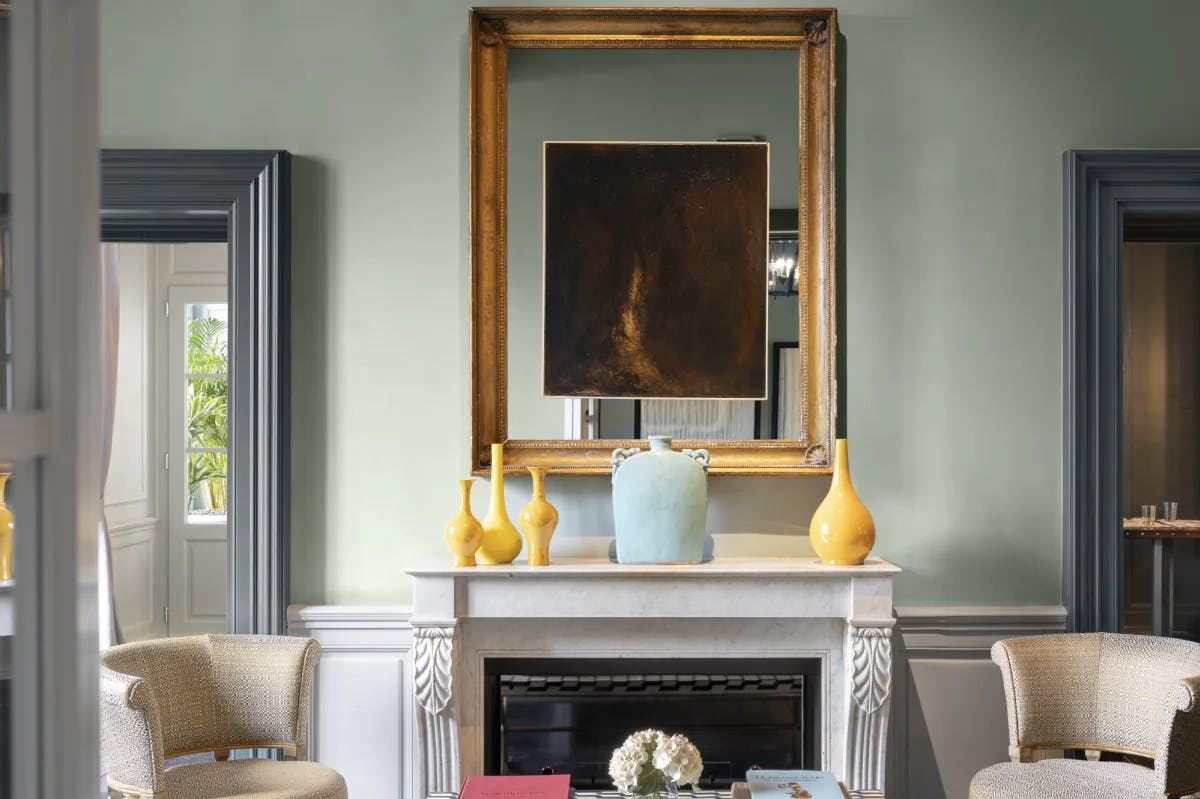 colorful vases rest on a luxe fireplace in front of a teal wall