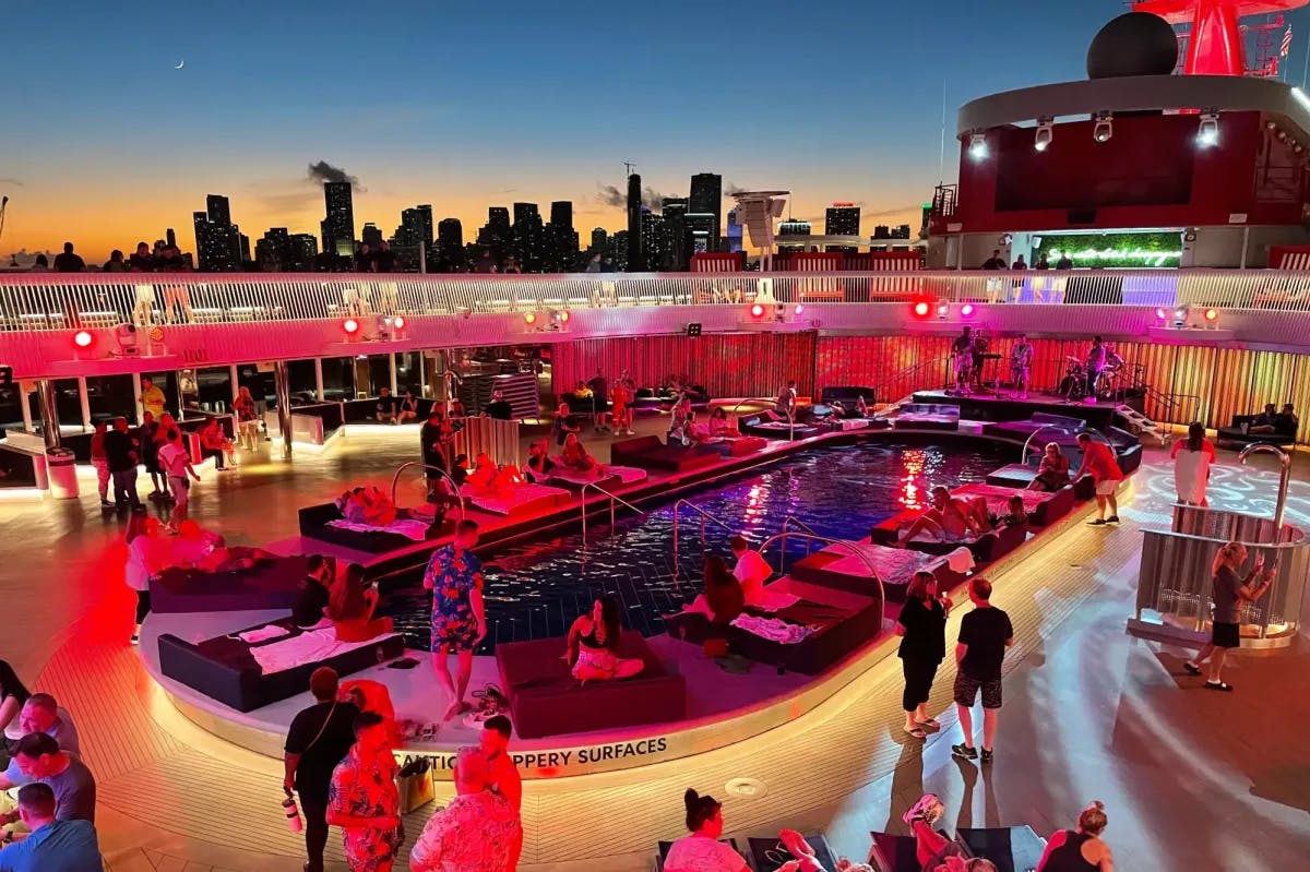 Pink-neon-lit pool deck on a Virgin Voyages cruise that's docked along an urban skyline