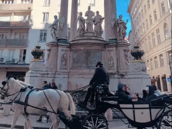 A horse carriage moving in front of a round about with statues.