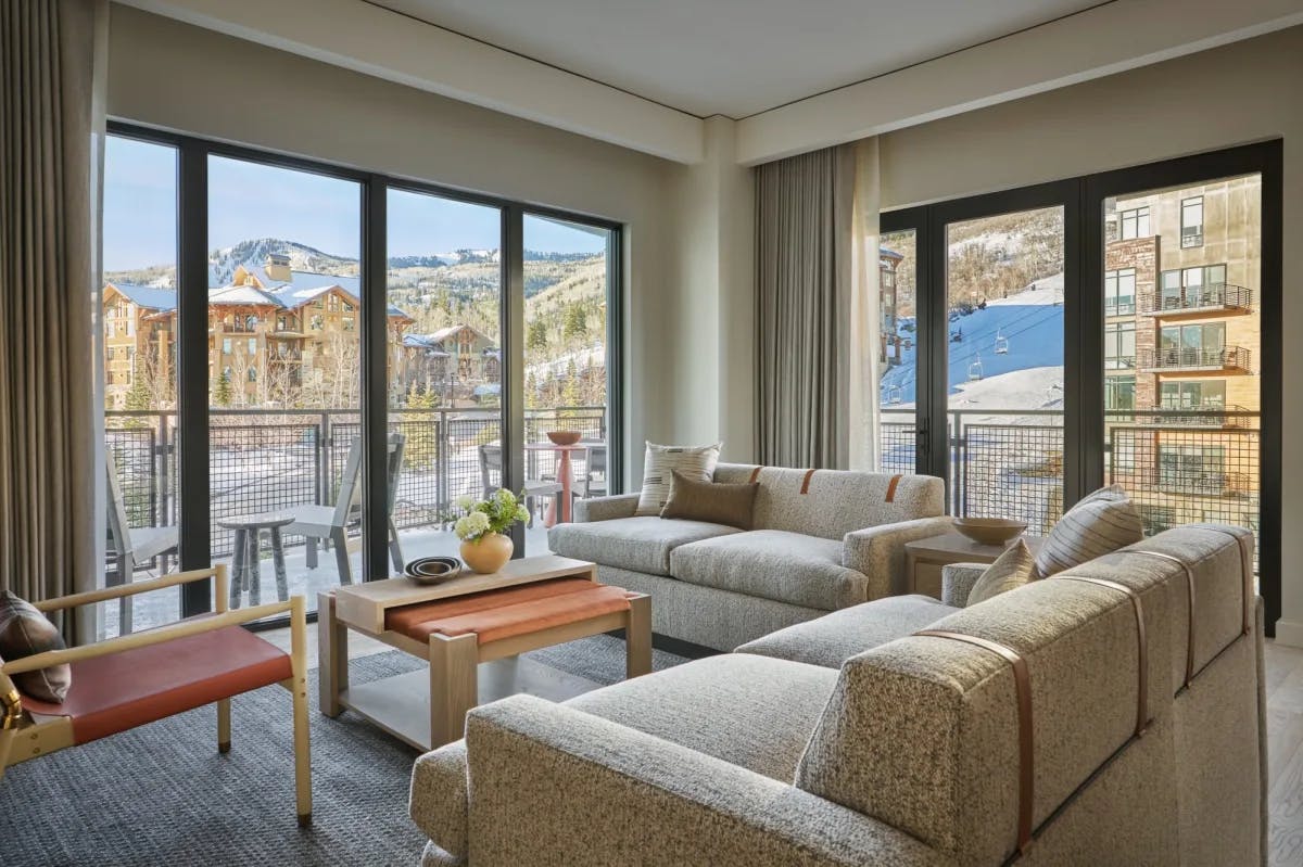 a fancy hotel room living area with tan couches overlooking a ski village