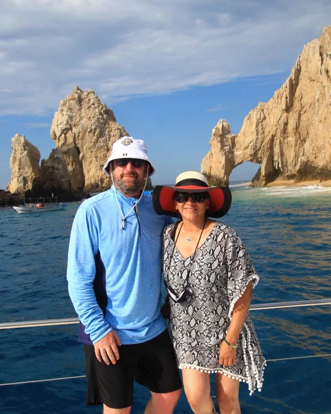 Travel advisor Lisa posing on the boat with husband in front of the Arch of Cabo San Lucas