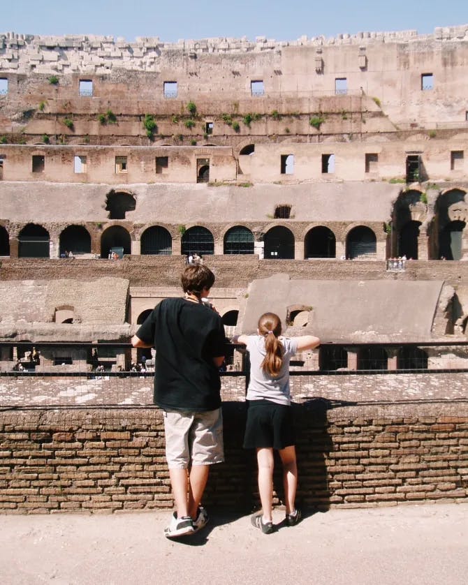 A photo of two people over looking a railing at a classic coliseum. 