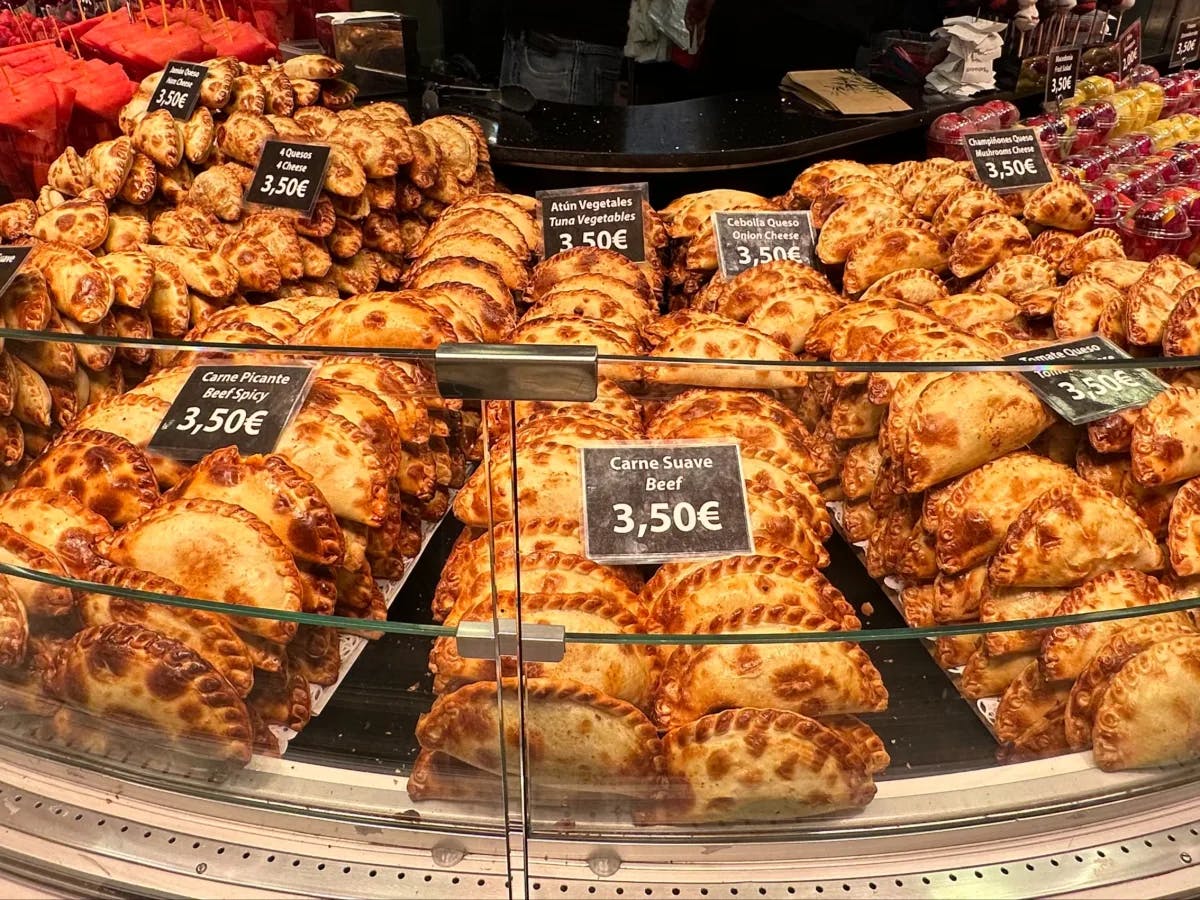 A glass case full of empanadas lined up in rows. There are black cards on top of them listing the price. 
