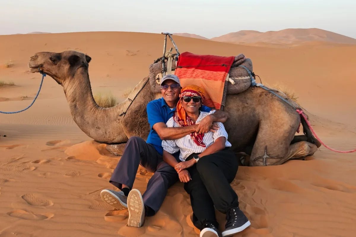 man and a woman sitting in front of a camel in a desert