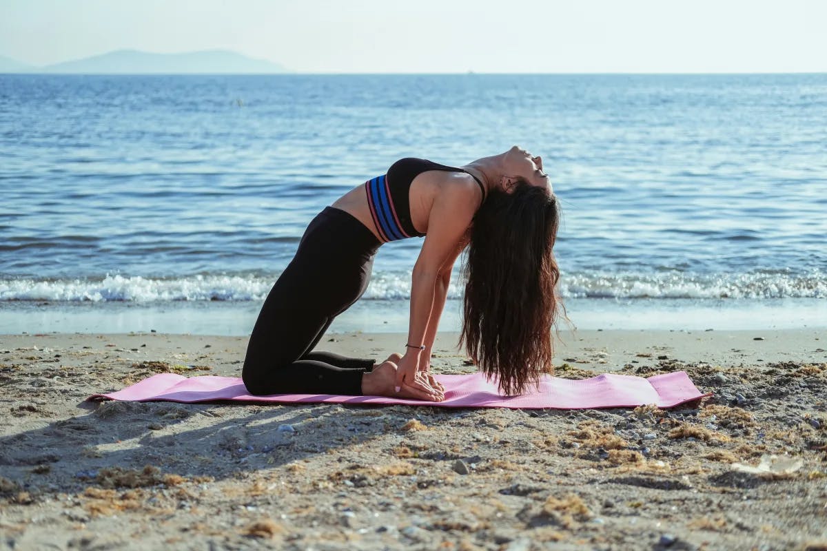 A picture of a girl doing a yoga pose near the beach.