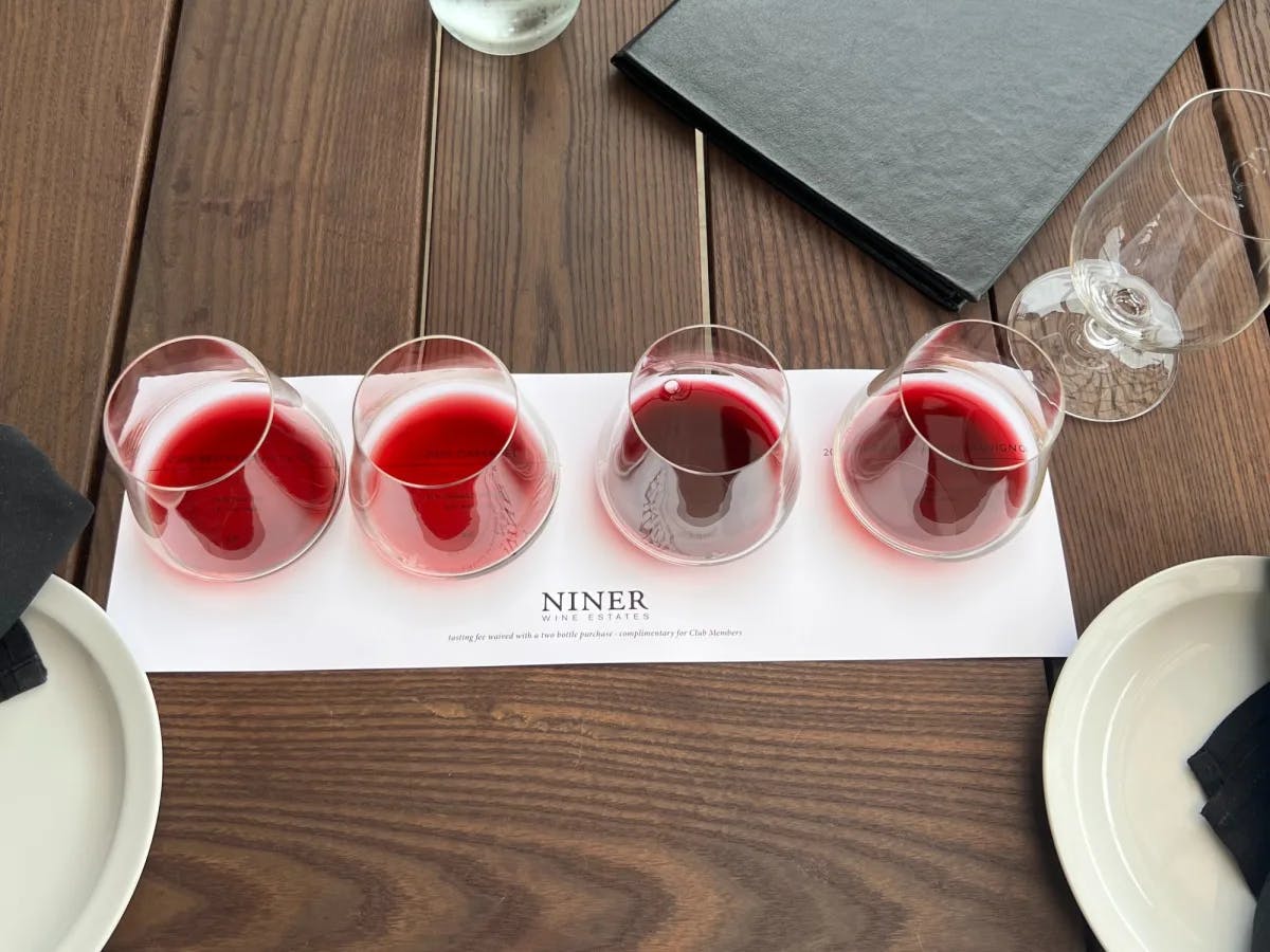 Four filled wine glasses on a white tray with NINER written on it. 