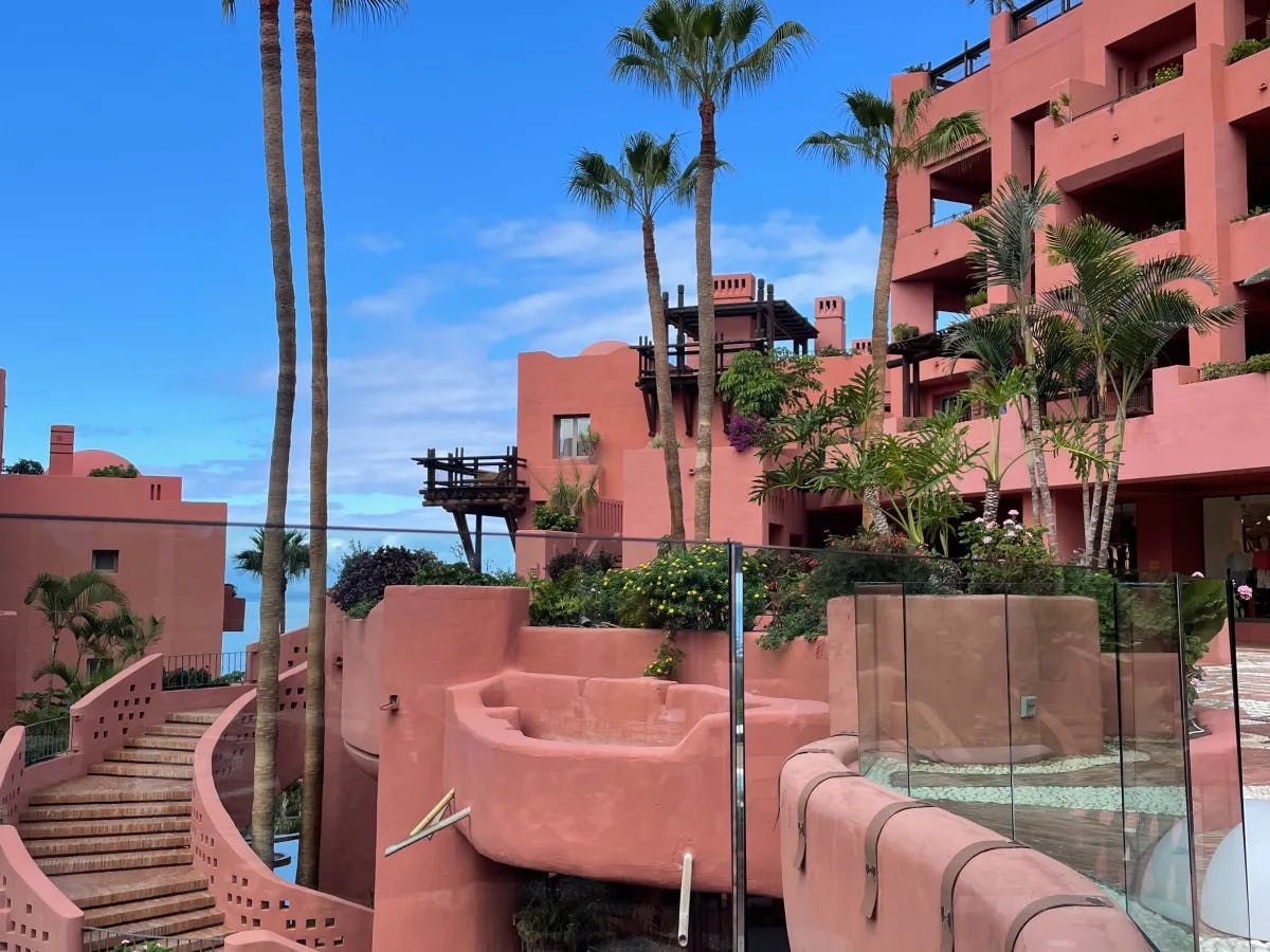 A view of a beautiful, pink building and palm trees in front of the bright blue sky. 