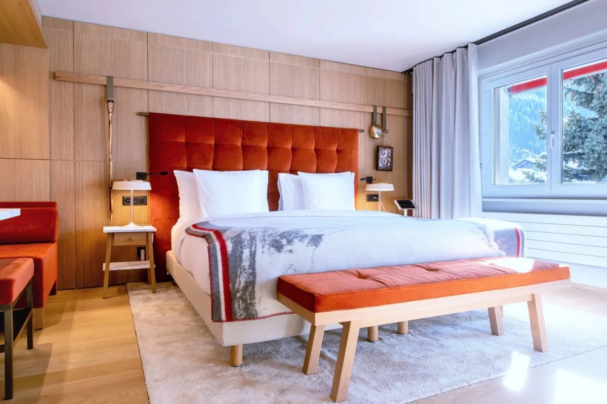 bedroom with white and orange bed and bench with a window looking out at trees