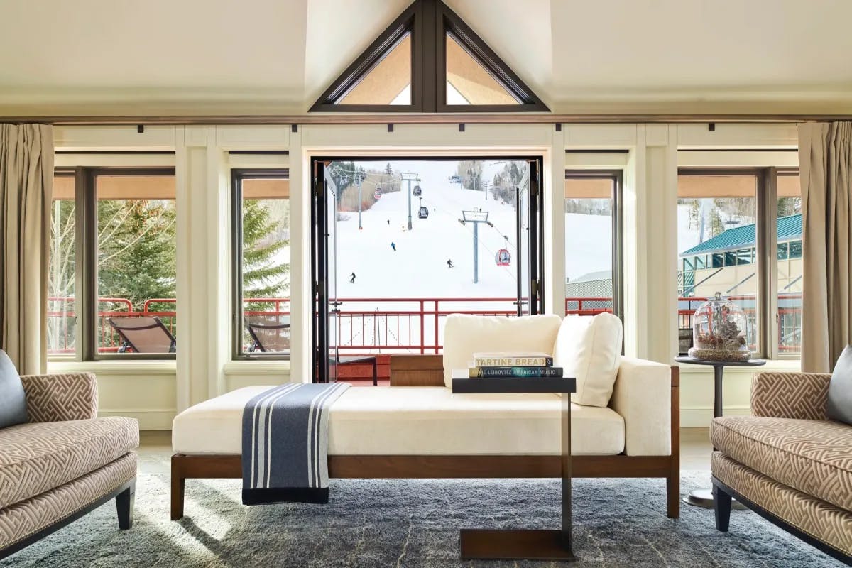 a sunlit hotel living room with a luxe white couch and large windows overlooking a ski mountain