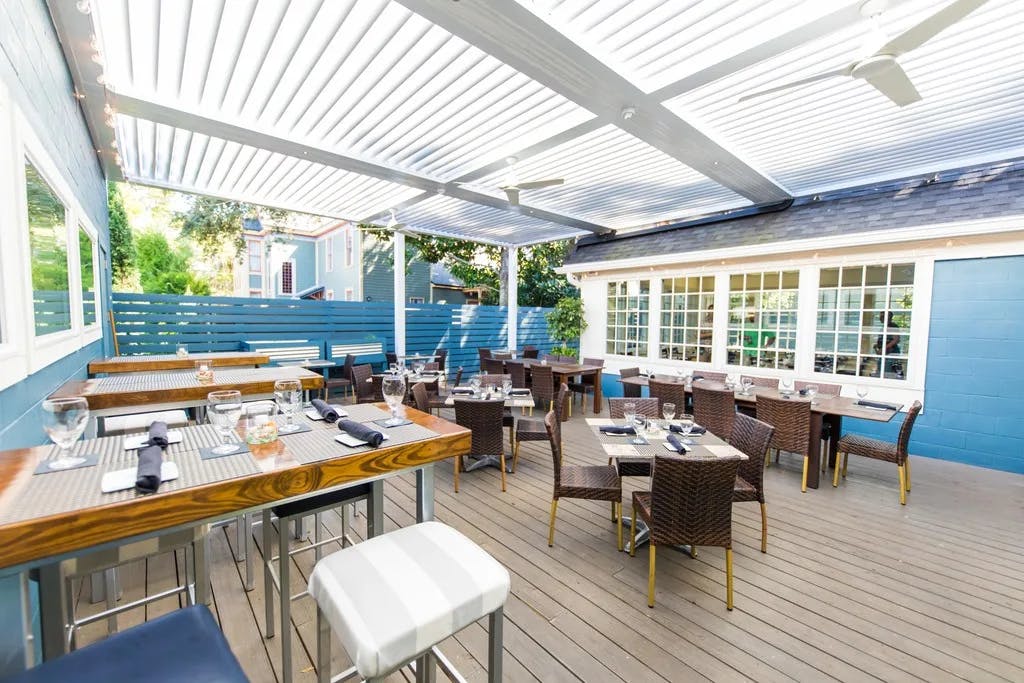 The covered terrace of a cozy restaurant with wooden deck flooring and blue walls at Burlingame Restaurant, Amelia Island.