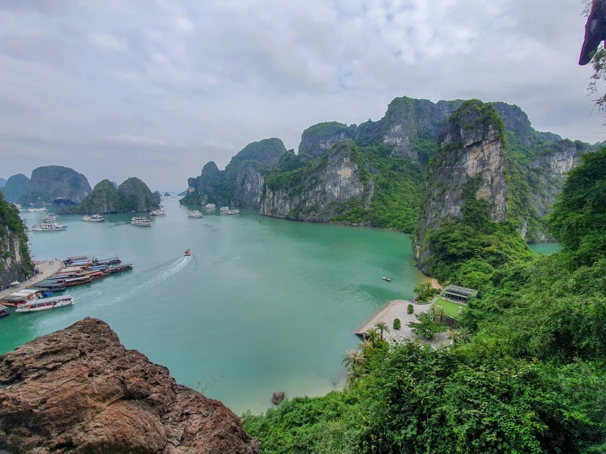 A view from above of Halong Bay with green-blue water, surrounded by rocky coastline and lush greenery.