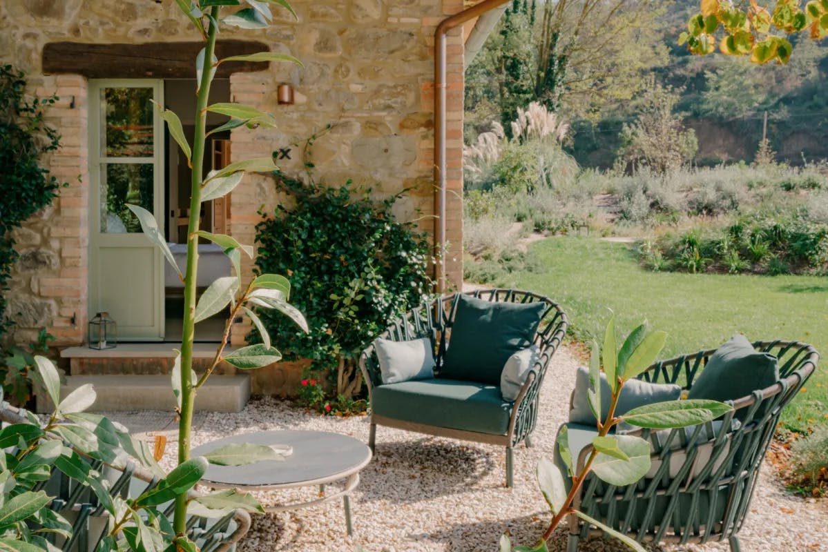 A pretty outdoor seating area by a garden and stone building with green furniture and plants.