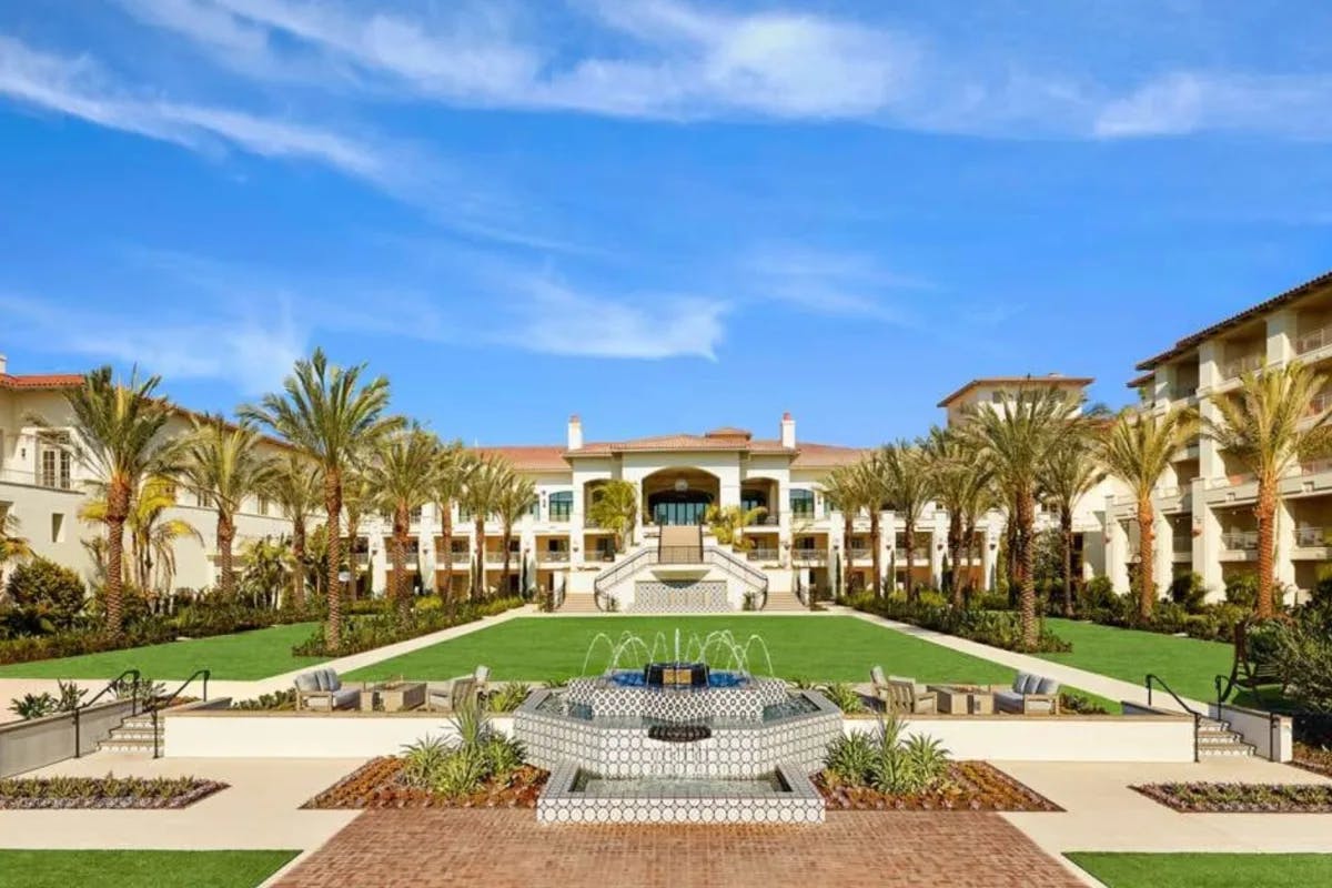 a hacienda-style hotel with a central lawn surrounded by palm trees with a blue sky