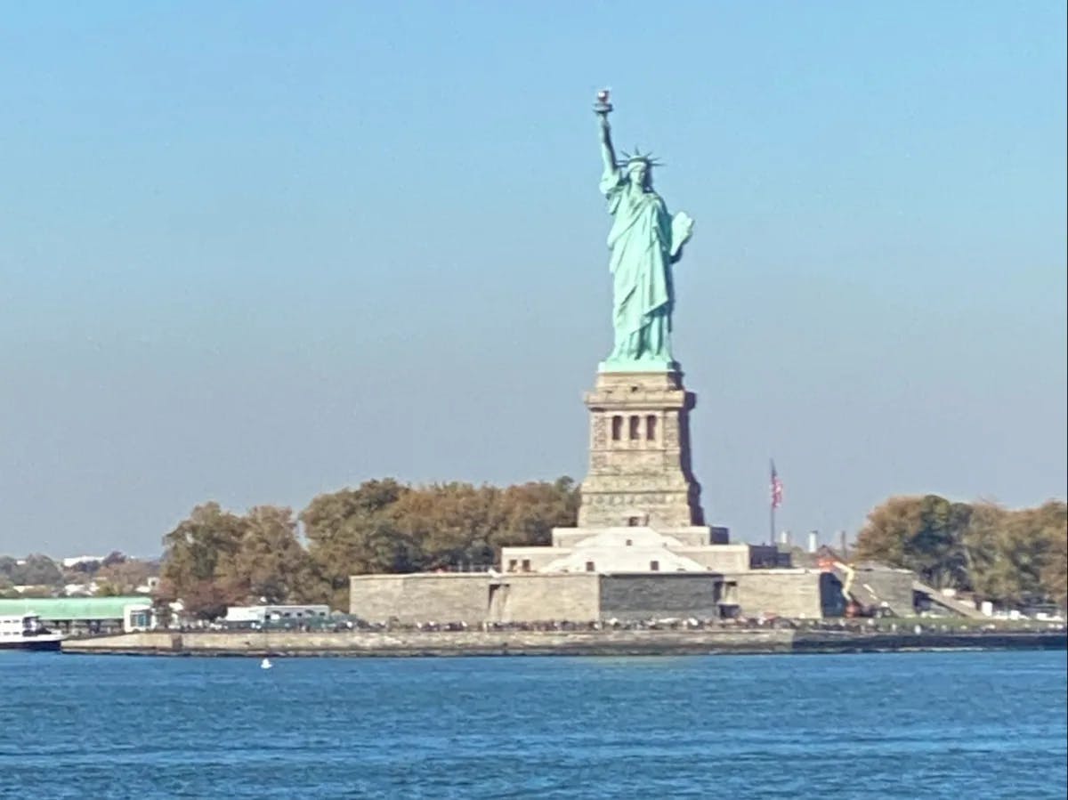 The Statue of Liberty standing tall against a clear blue sky, as seen from across water.