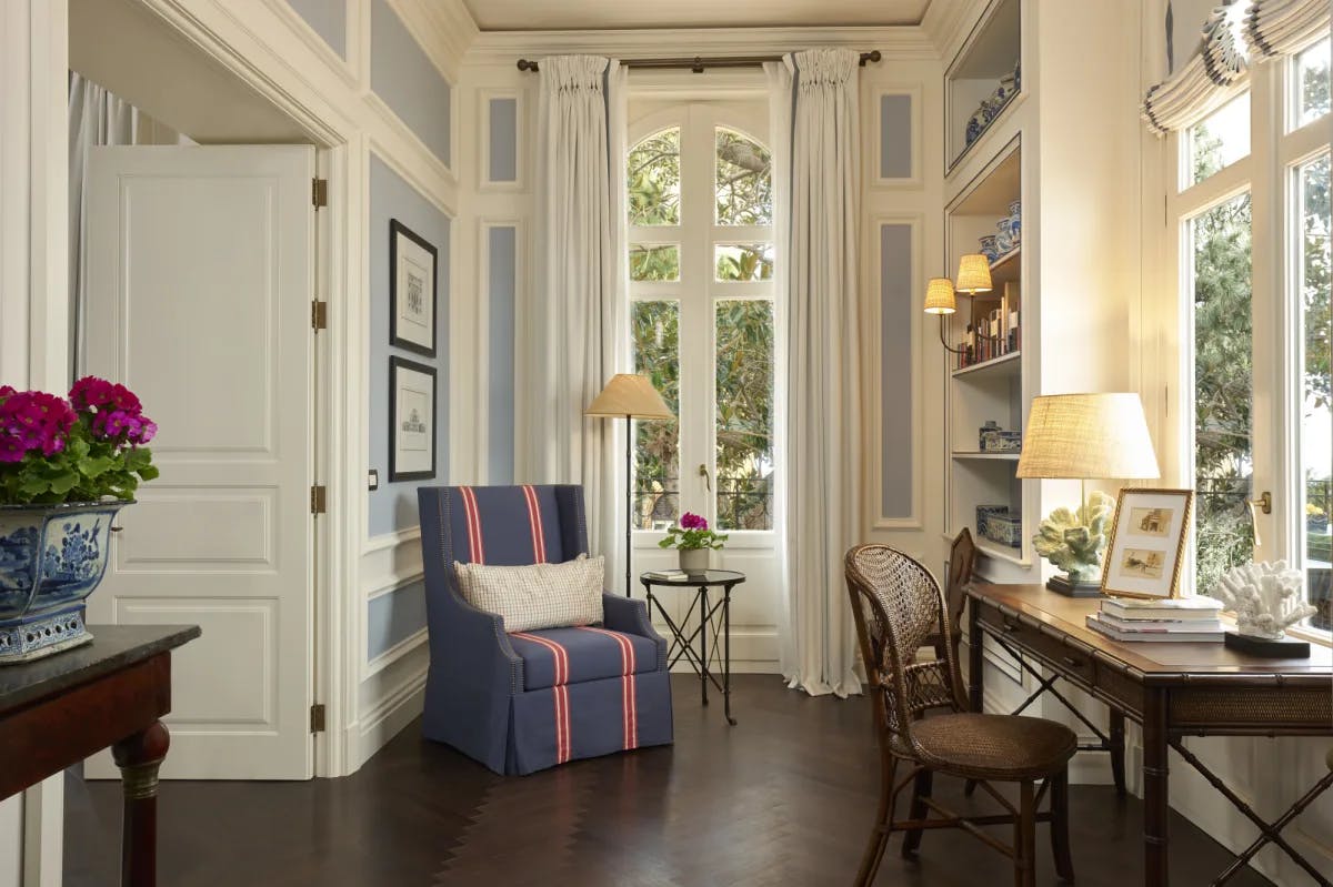 a handsome writing room with towering windows and a comfy upholstered chair