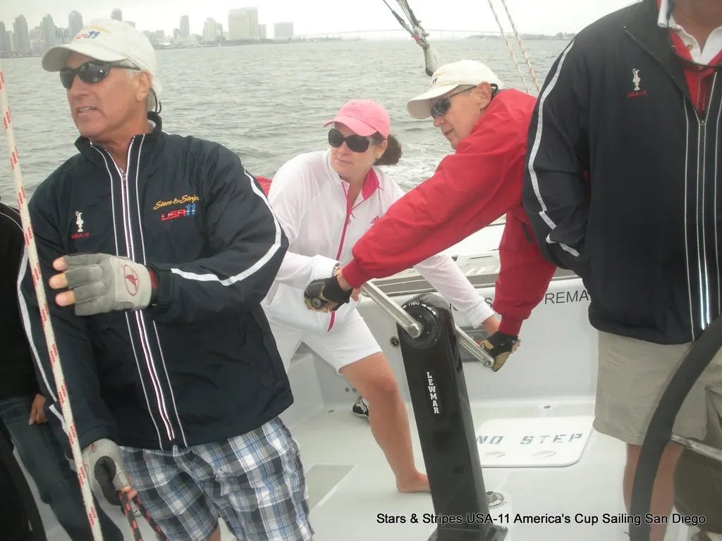 A group of people in hats and sunglasses operating a sailboat on the harbor.